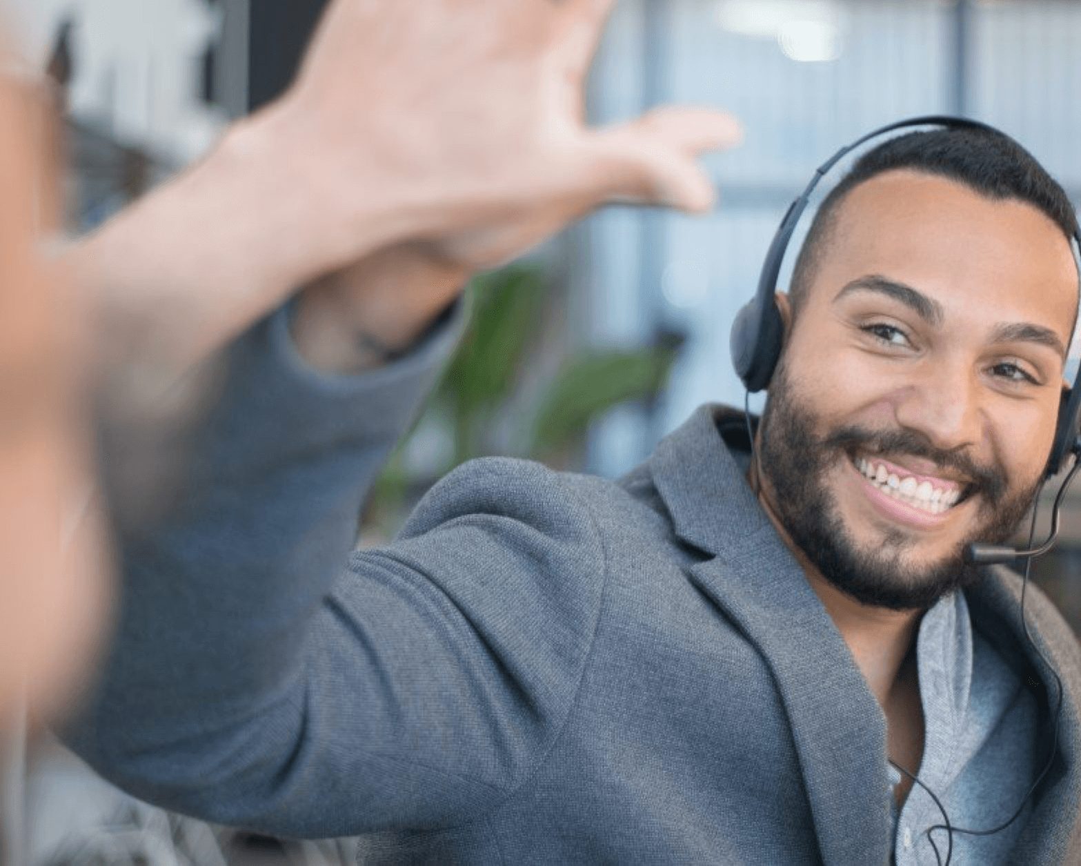 A bearded young man with a headset on his head giving someone a high-five while smiling brightly.